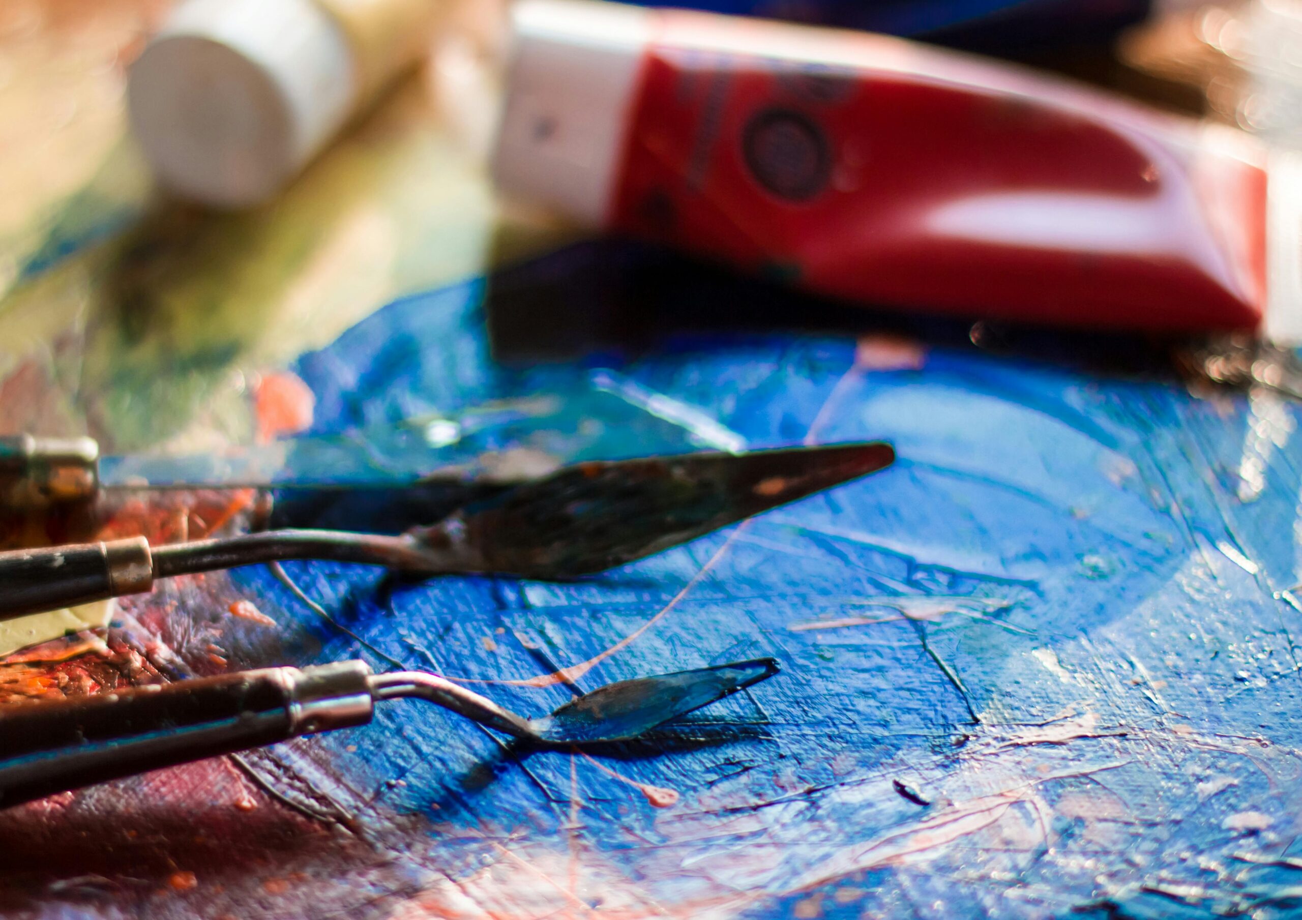 two palette knifes rest on a glass panel covered in blue paint