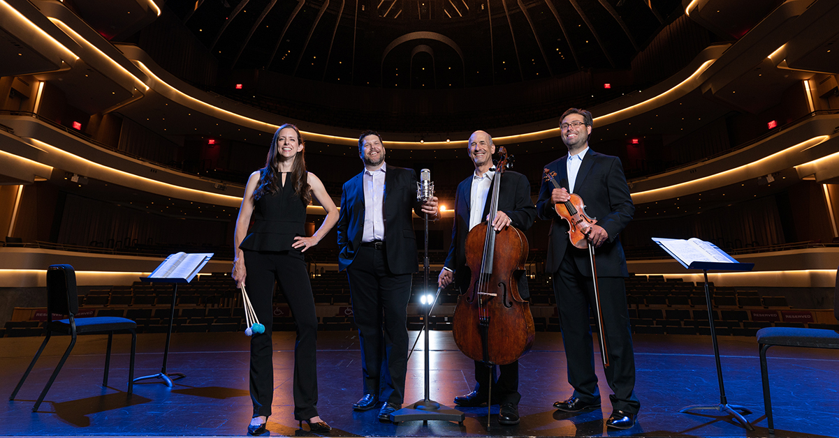 A classical music quartet standing on a large stage with their musical instruments