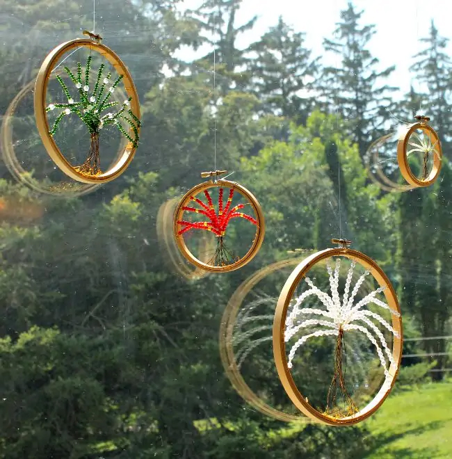 Four round frames with beads arranged to look like trees come together to make suncatchers that are displayed in a sunny window